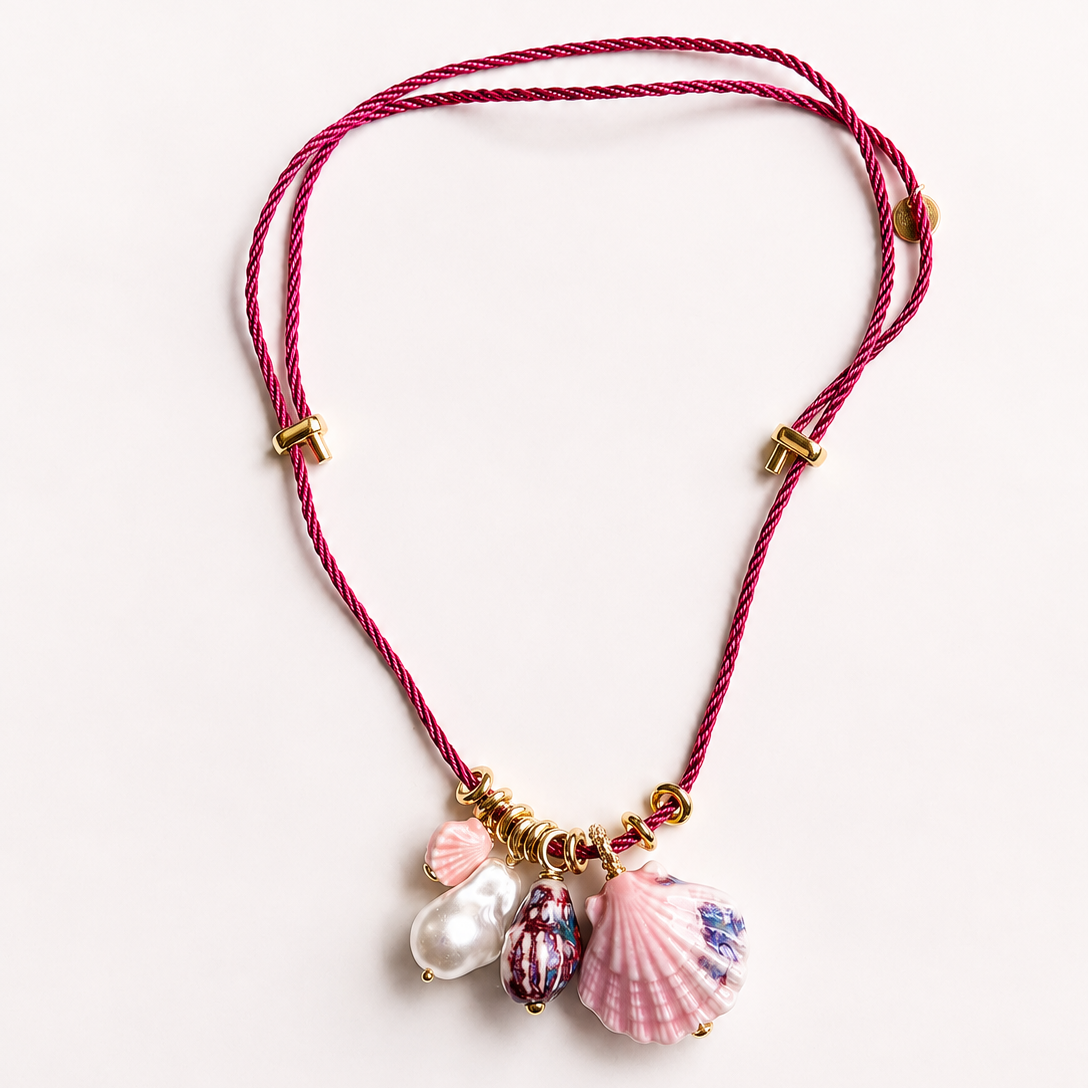 Necklace with shell and pearl charms on a pink cord against a white background