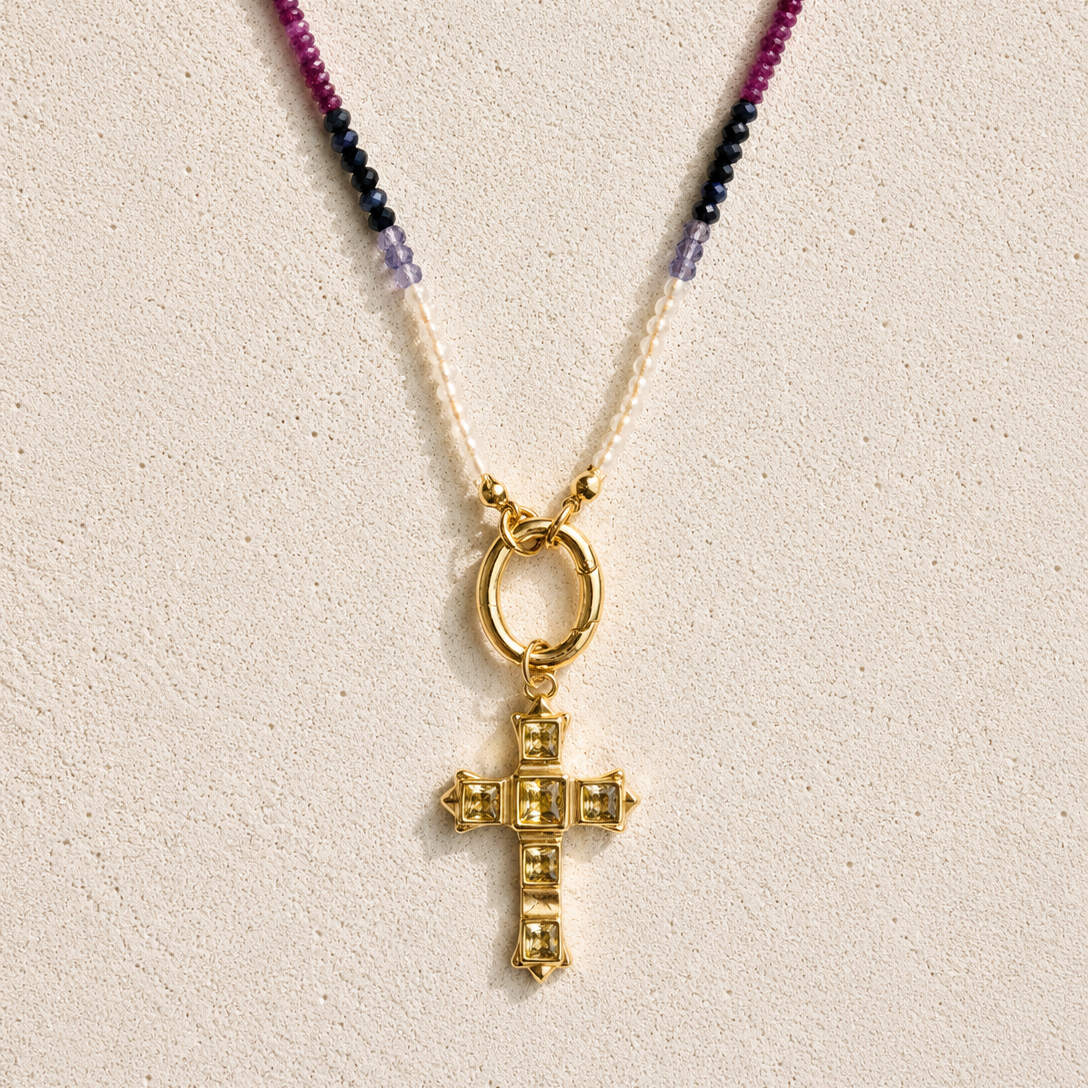 Gold cross pendant necklace with colorful beads on a beige background