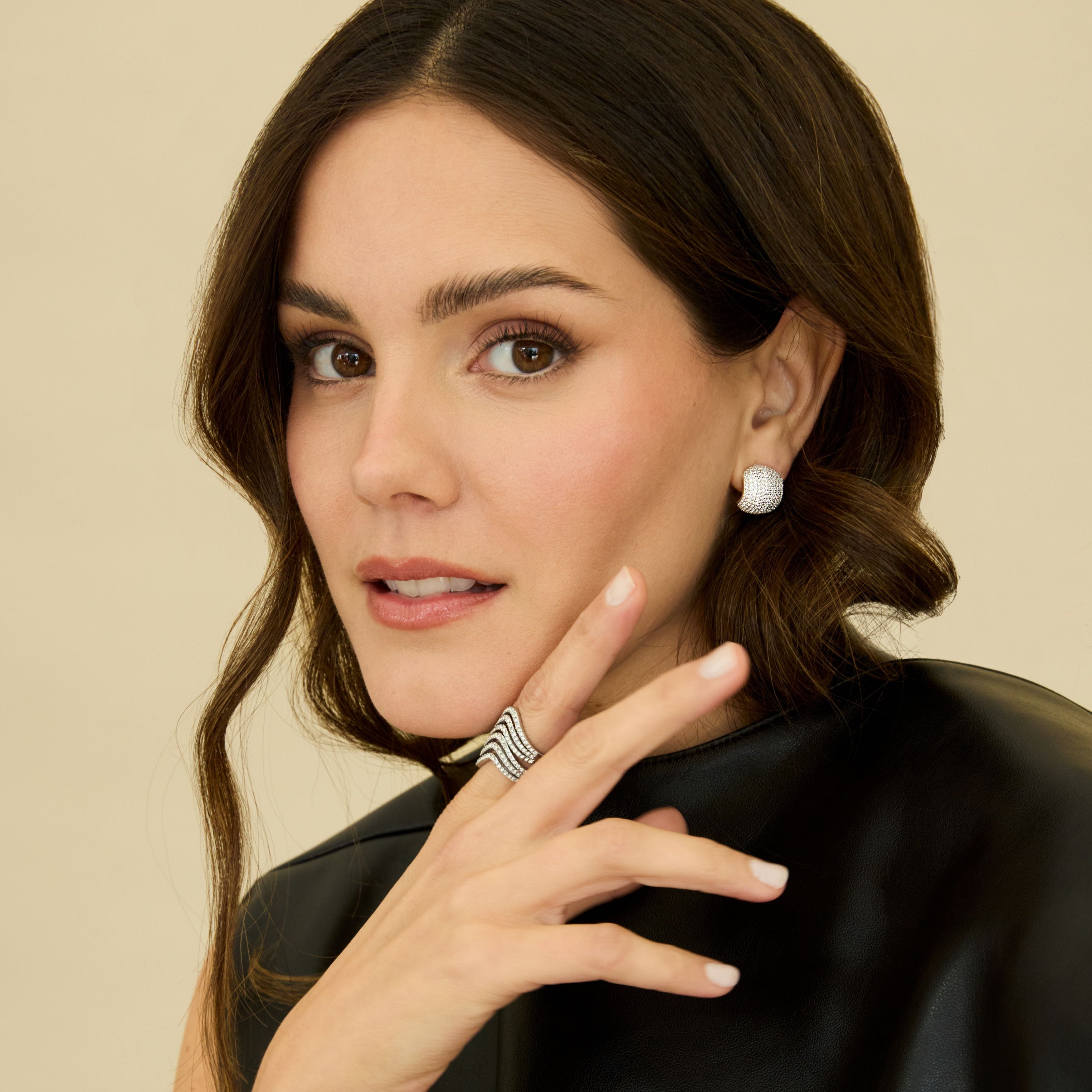 Woman wearing jewelry including earrings, a ring, and a bracelet against a beige background