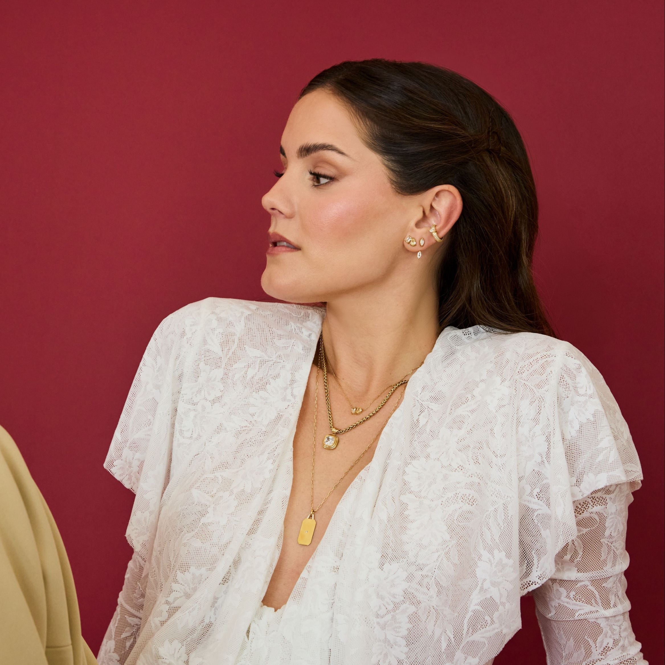 Woman wearing a white lace top and beige pants against a red background