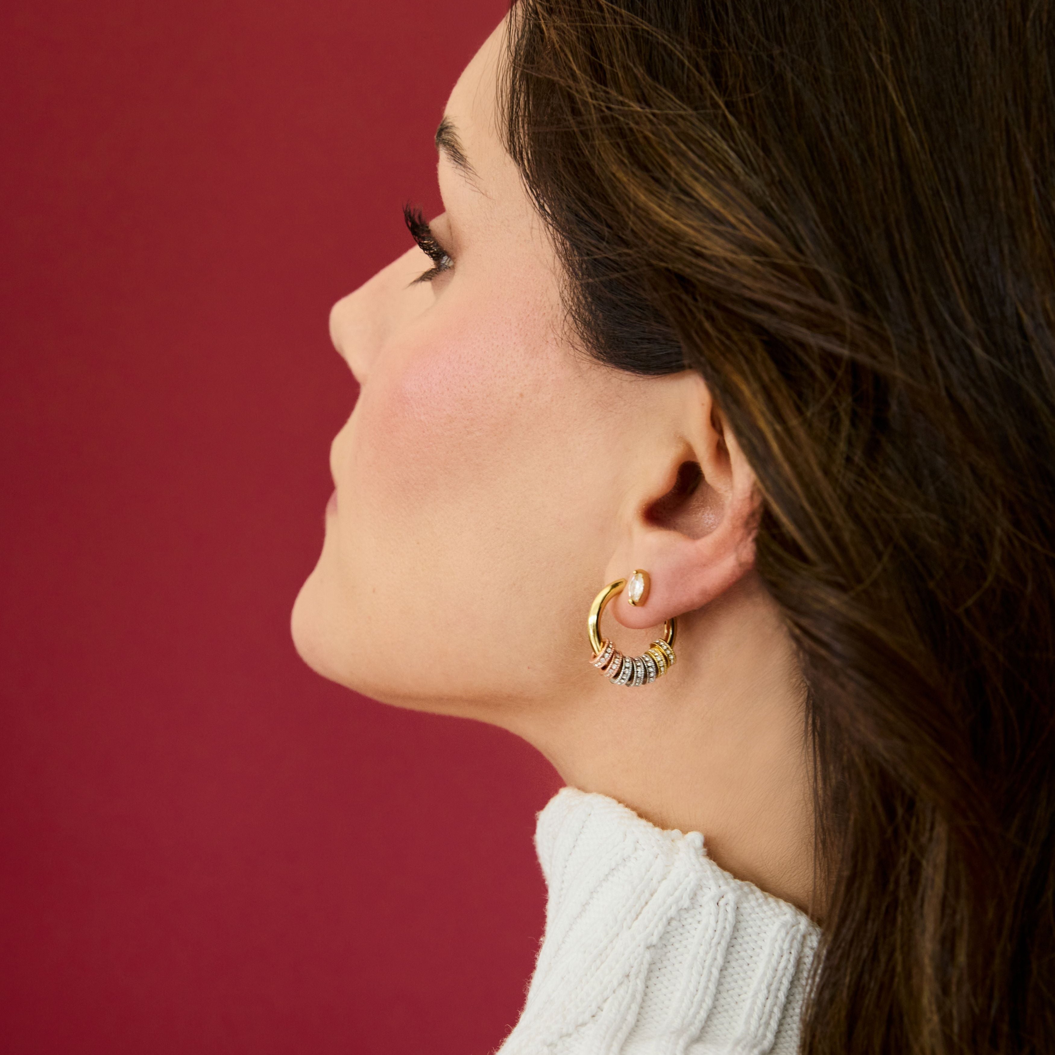 Woman wearing gold hoop earrings against a red background